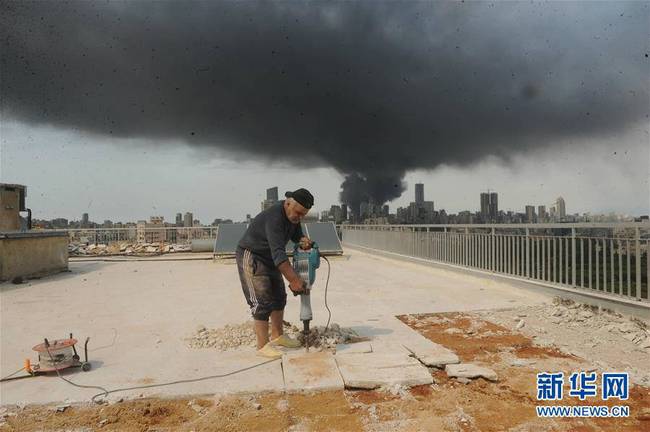 9月10日，在黎巴嫩首都贝鲁特，一名正在施工的建筑工人身后是港口区一处仓库起火后产生的浓烟。