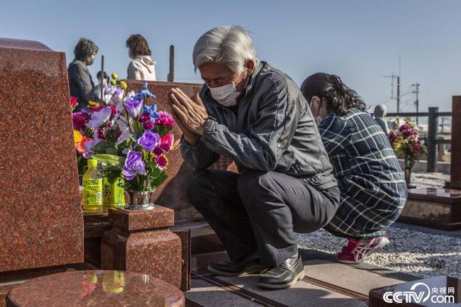 当地时间2021年3月11日，日本福岛县浪江町，一名在地震中失去家人的幸存者在墓碑前默哀祈祷。